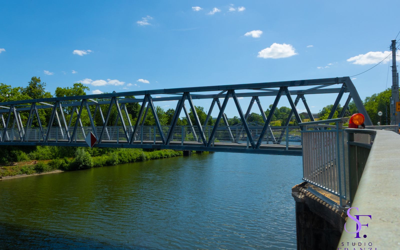 Stahlbrücke über einen Fluss bei sonnigem Wetter mit blauem Himmel.