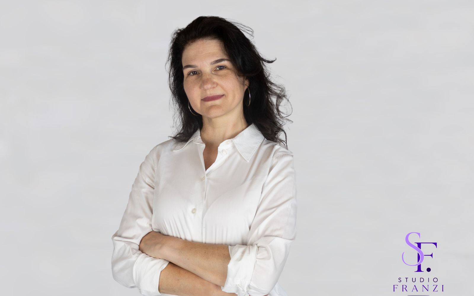 Businessportrait einer Frau mit weißer Bluse und verschränkten Armen vor hellem Hintergrund.