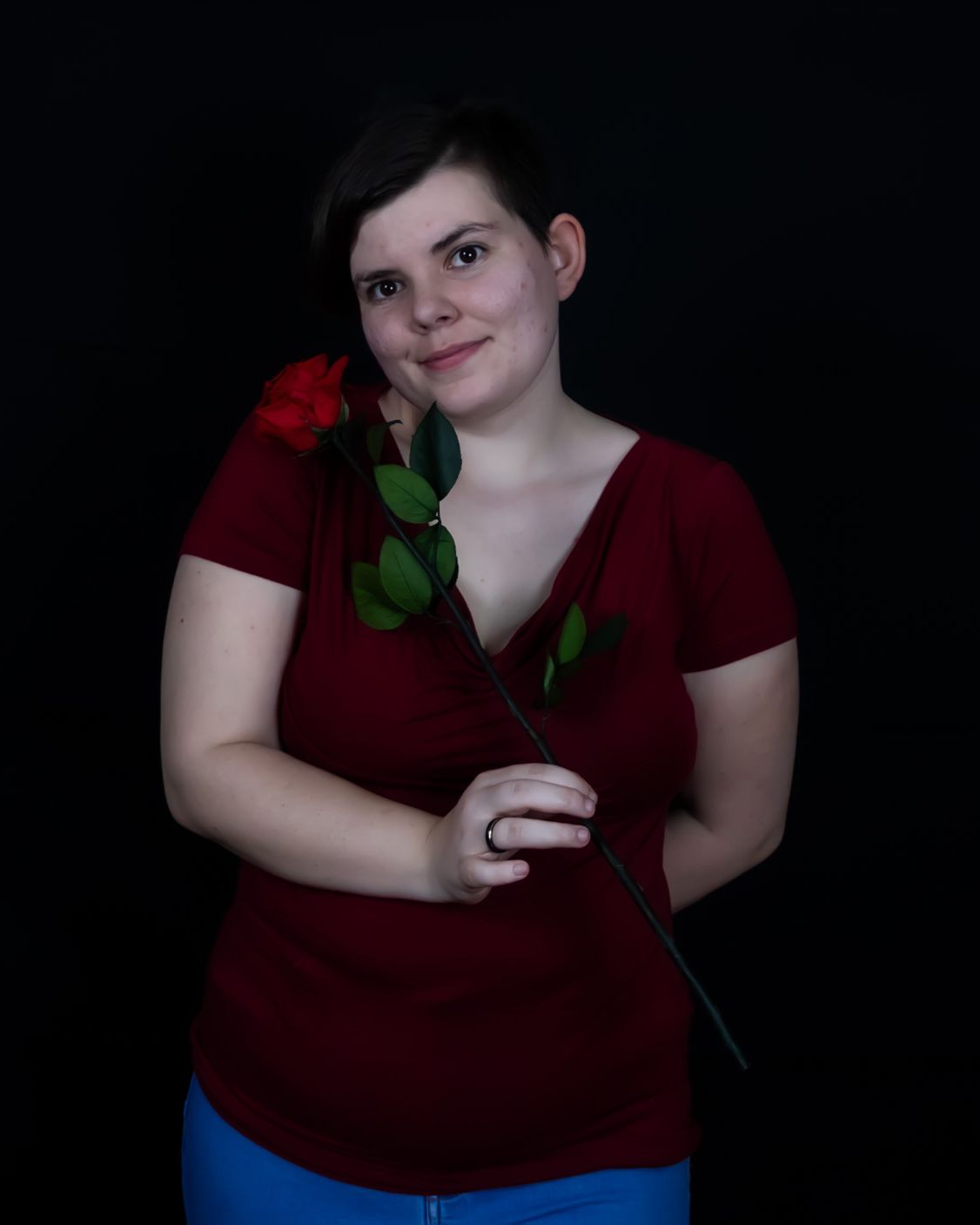 Portrait einer lächelnden Frau mit einer roten Rose vor schwarzem Hintergrund.
